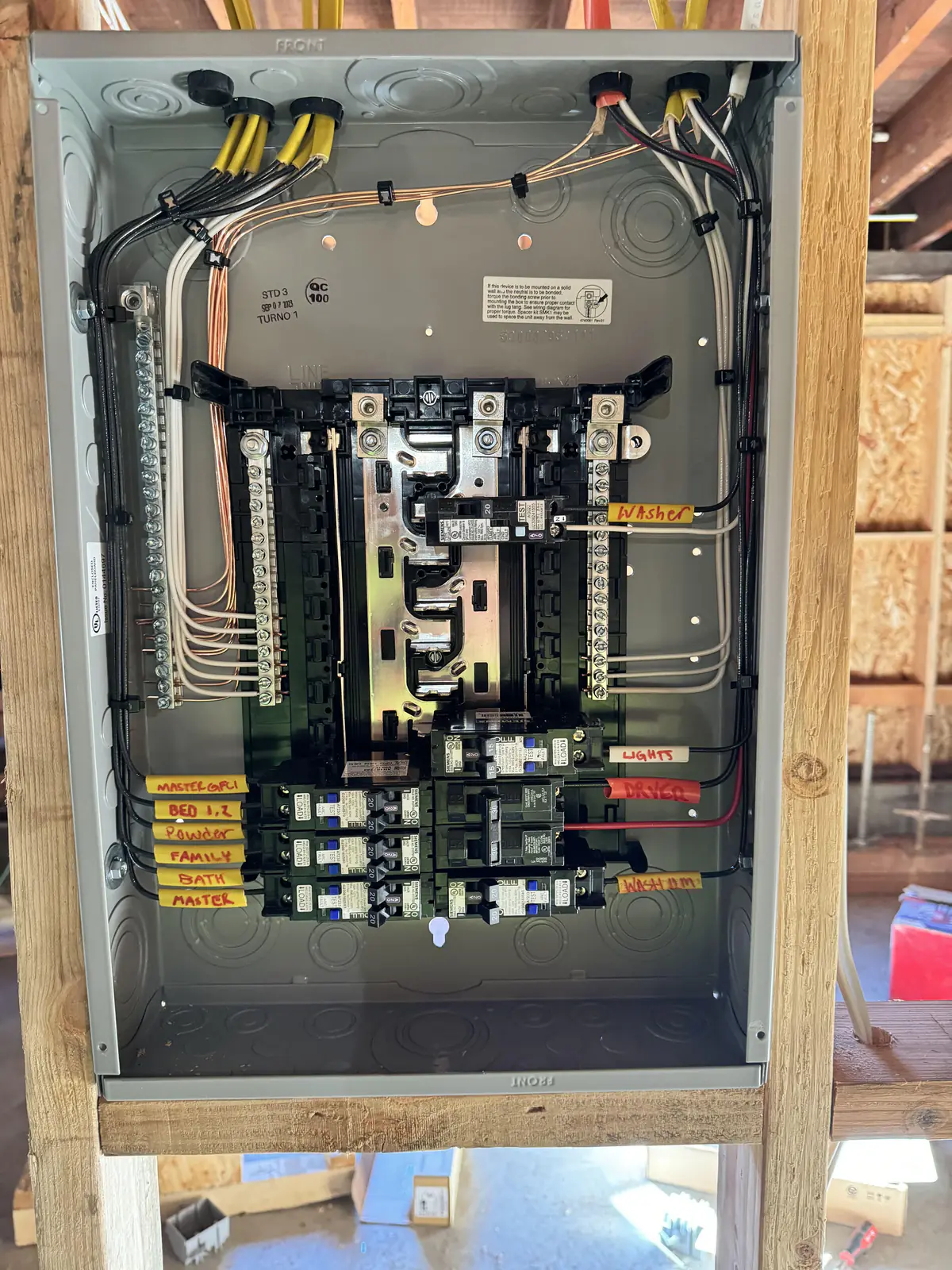 Open electrical panel with labeled breakers and neatly routed wires between wall studs